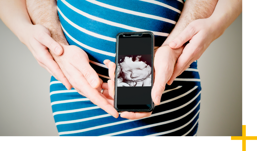 Foto einer schwangeren Person, die ein Ultraschallbilld ihres Babys vor ihrem Bauch hält